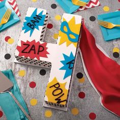 a table topped with cake and napkins covered in comic themed icing next to utensils