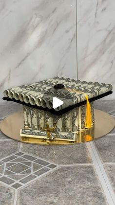 a graduation cap made out of money sitting on top of a marble floor next to a white wall