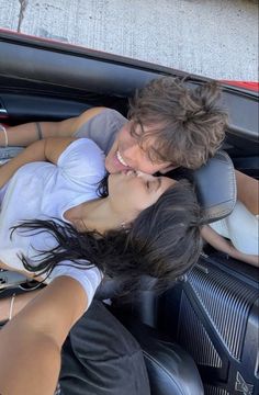 two people sitting in the back seat of a car, one is kissing the other