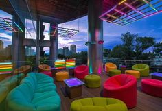 brightly colored chairs and tables on a wooden floor in front of large windows with city lights