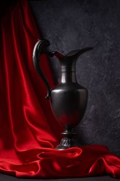 a silver vase sitting on top of a red cloth covered table next to a black wall