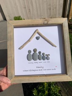 a person holding up a frame with rocks in the shape of a house and family