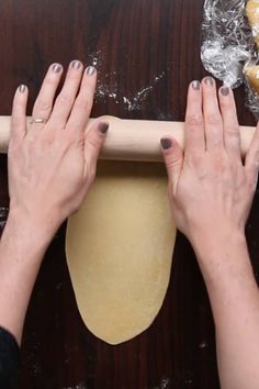 two hands are rolling dough on a wooden table