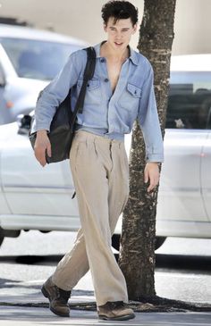 a man walking down the street with a handbag on his shoulder and wearing pants