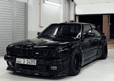 a black car parked in a garage next to a white wall and some metal doors