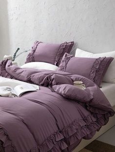 a bed with purple ruffled sheets and pillows