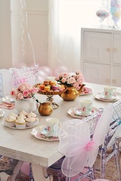 the table is set with tea cups, plates and cupcakes for two people