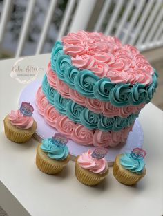 there is a large cake with pink and blue frosting on the top, surrounded by cupcakes