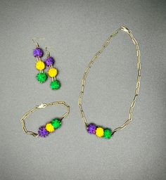 Mardi Gras Metallic Pom Pom Jewelry Set. Purple, Green and Gold lightweight Pom Poms paired with 18k gold platted stainless steel.  Set includes: Short necklace (@ 16.5 inches) Bracelet (@ 8 inches) Earrings (@ 2.75 inches from lob) Pieces are available as a set or individually Party Jewelry With Yellow Ear Wire, Yellow Jewelry With Ear Wire For Party, Yellow Adjustable Bracelet, Yellow Adjustable Chain Bracelet, Multicolor Jewelry With Dangle Adjustable Chain, Multicolor Brass Jewelry For Celebration, Yellow Jewelry With Matching Earrings For Celebration, Multicolor Brass Jewelry For Gift, Yellow Brass Dangle Jewelry