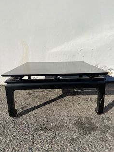 a black coffee table sitting on top of a cement floor next to a white wall