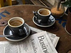 two cups of coffee sit on top of newspapers