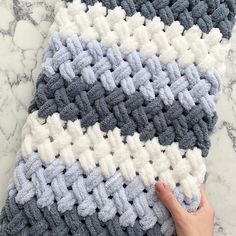 someone is crocheting a blue and white blanket on the floor with their hand