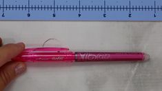 a person holding a pink pen in front of a ruler