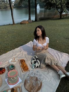 a woman sitting on top of a blanket next to a table filled with cakes and desserts