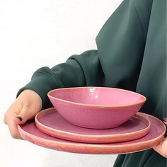 a person holding two pink plates and a bowl on their arm, with the other plate in front of them