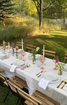 a long table with plates and place settings on it in the middle of a grassy area