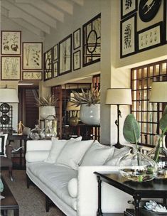 a living room filled with white furniture and pictures on the wall above it's windows