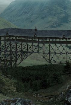 a train crossing over a bridge with mountains in the background and foggy skies above