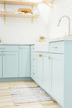 a kitchen with light blue cabinets and white counters, gold pulls on the faucet