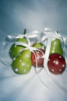 three apples and two pears tied together with white ribbons on a bed sheet,