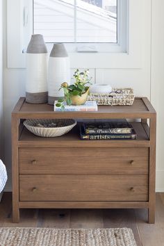 a wooden dresser with two vases and books on it in front of a window