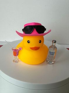 a yellow rubber duck with sunglasses and a pink hat on top of a white table