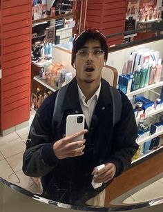 a man holding a cell phone in front of a display case at a cosmetics store