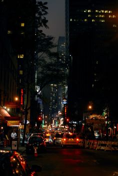 a city street at night with cars parked on the side and tall buildings in the background