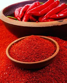 red chili powder in a bowl next to a wooden spoon with peppers on the side