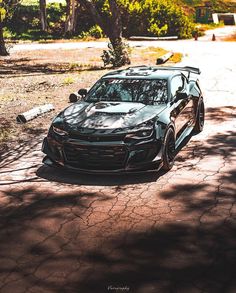 a car parked on the side of a road next to some trees and dirt ground