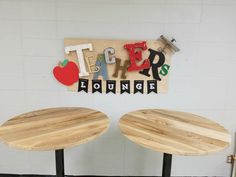 two wooden tables sitting next to each other in front of a white wall with letters on it