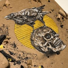 a drawing of a skull and a crow on a piece of cardboard with yellow paint