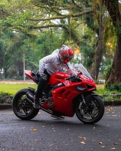 a man riding on the back of a red motorcycle down a street next to trees