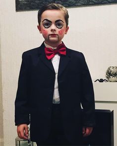 a young boy dressed up in a suit and red bow tie with makeup on his face