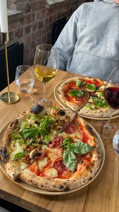 two pizzas sitting on top of a wooden table next to wine glasses and a candle