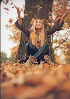 a woman sitting on the ground in front of a tree with her arms outstretched up