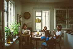 a group of people sitting around a wooden table in a room with white walls and windows