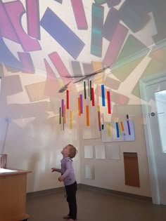 a little boy standing in front of a wall with colorful art on it's walls