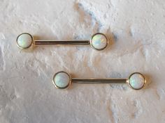 two opal barbell piercings on a marble surface