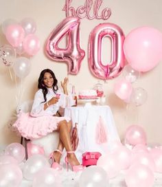 a woman sitting in front of a table with pink and white balloons on top of it