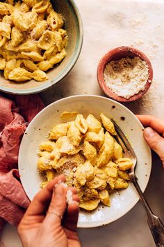 two hands holding a bowl of macaroni and cheese next to bowls of flour