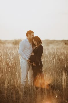 a pregnant couple cuddles in the tall grass