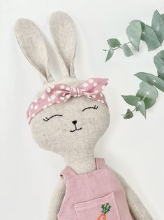 a stuffed rabbit with a pink bow on it's head sitting next to some green leaves