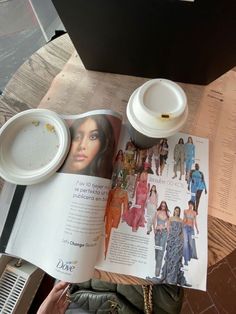 an open magazine sitting on top of a wooden table next to a cup of coffee