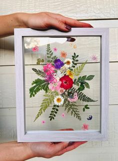 a person holding up a frame with flowers on it