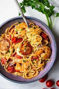 pasta with shrimp and tomatoes in a blue bowl on a white tablecloth next to a fork