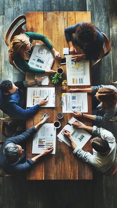 four people sitting at a table with papers and pens in their hands, looking down on them