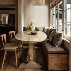 a wooden table sitting in front of a window next to a bench with pillows on it