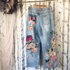 a pair of blue jeans with flowers on them hanging from a clothes line in front of a wall