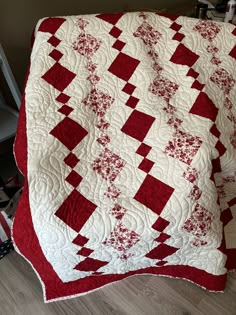 a large red and white quilt on top of a wooden floor next to a chair